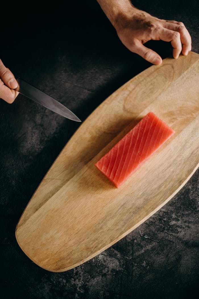 Close-up of fresh tuna being prepared with a knife on a wooden board.
